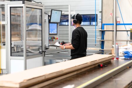 En anställd övervakar och styr en maskin via ett digitalt gränssnitt i en modern fabriksmiljö.