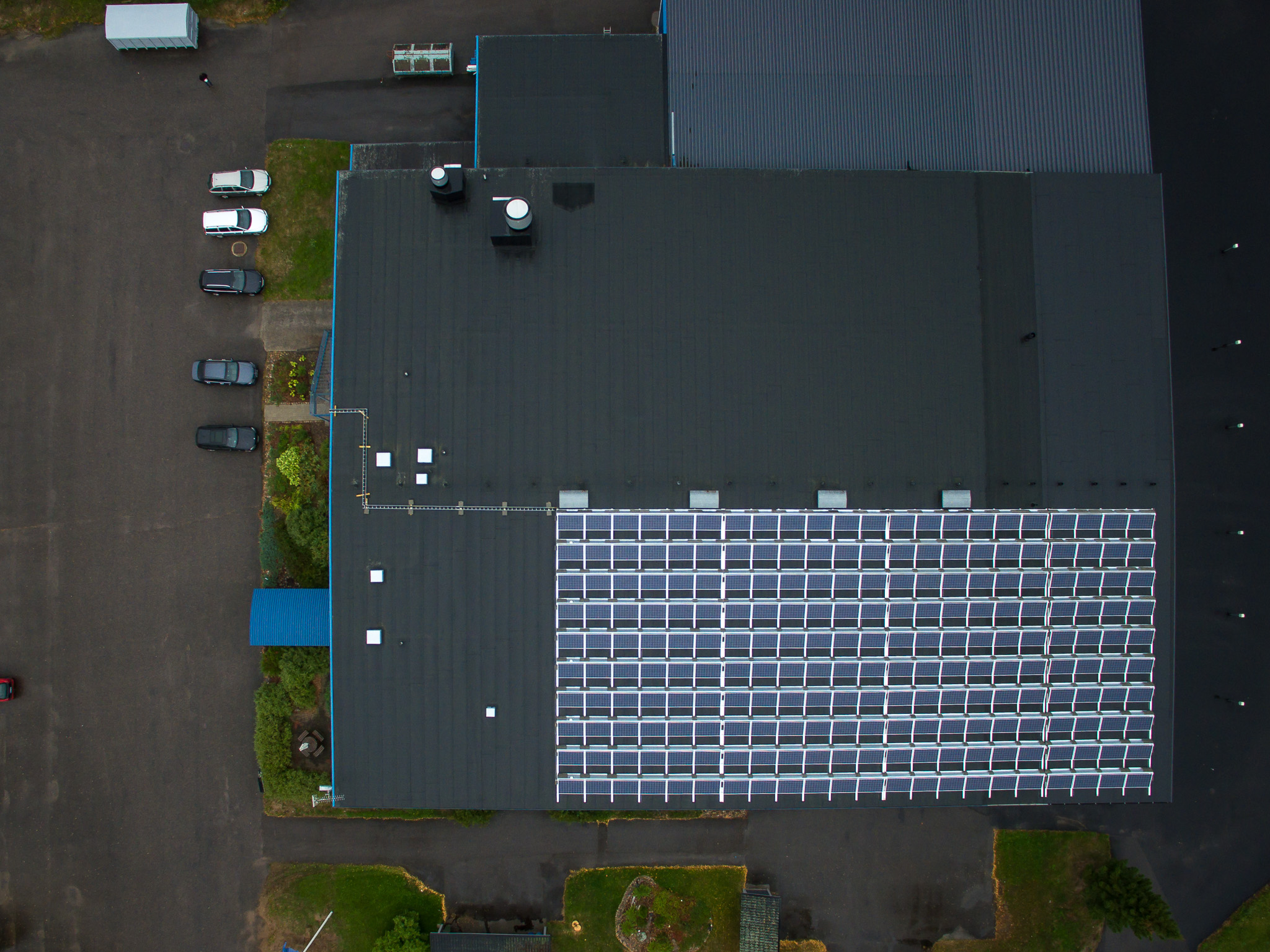 En drönarbild tagen uppifrån av en industrianläggning med solpaneler på taket, som lyfter fram hållbar energianvändning.