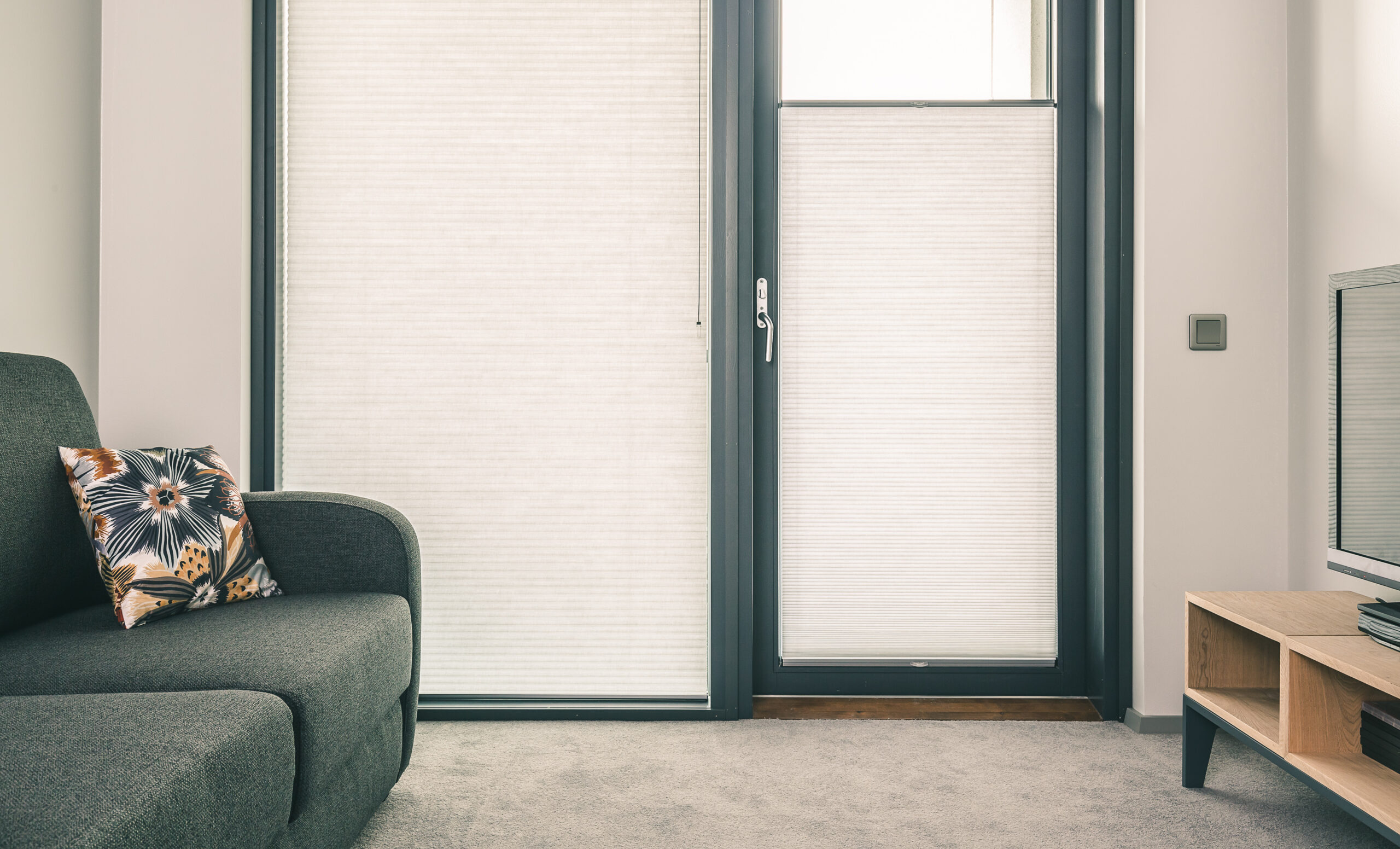 Cozy interior with armchair and glass door, featuring pleated blinds that filter light and create a calm atmosphere.