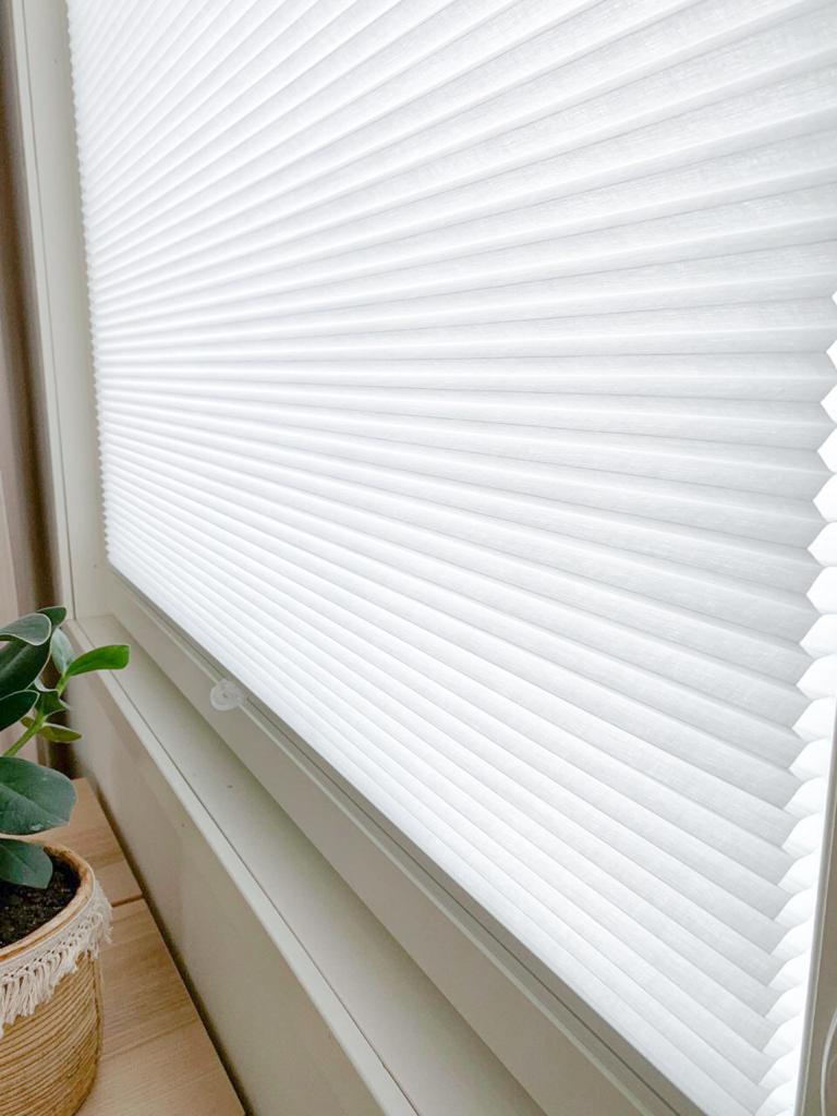 Närbild på en ljusreglerande plisségard som är monterad på ett fönster, där de strukturerade veckningarna och den rena, minimalistiska designen framhävs.