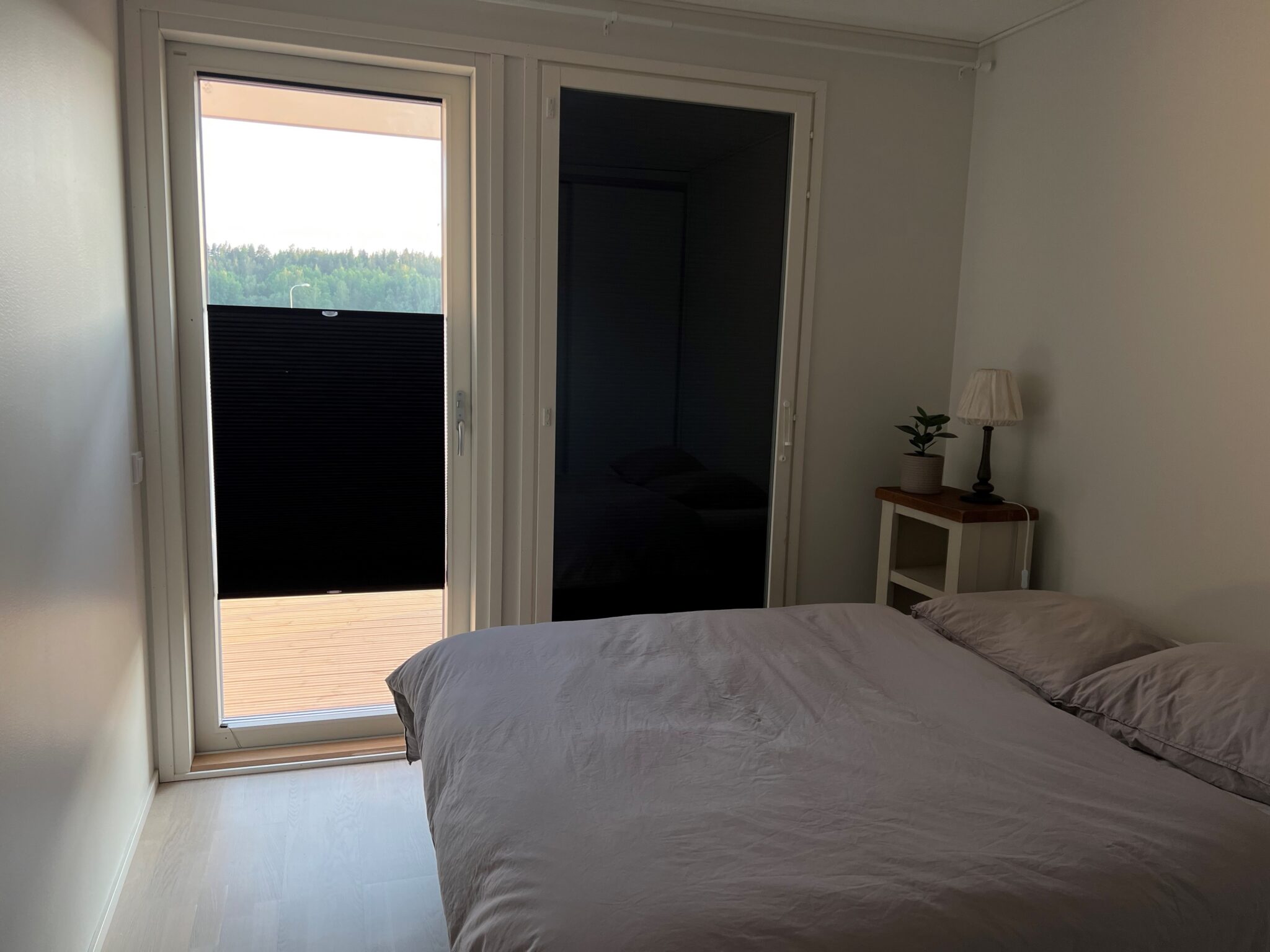 Bedroom with balcony doors fitted with dark pleated blinds, creating a dim and restful sleeping environment