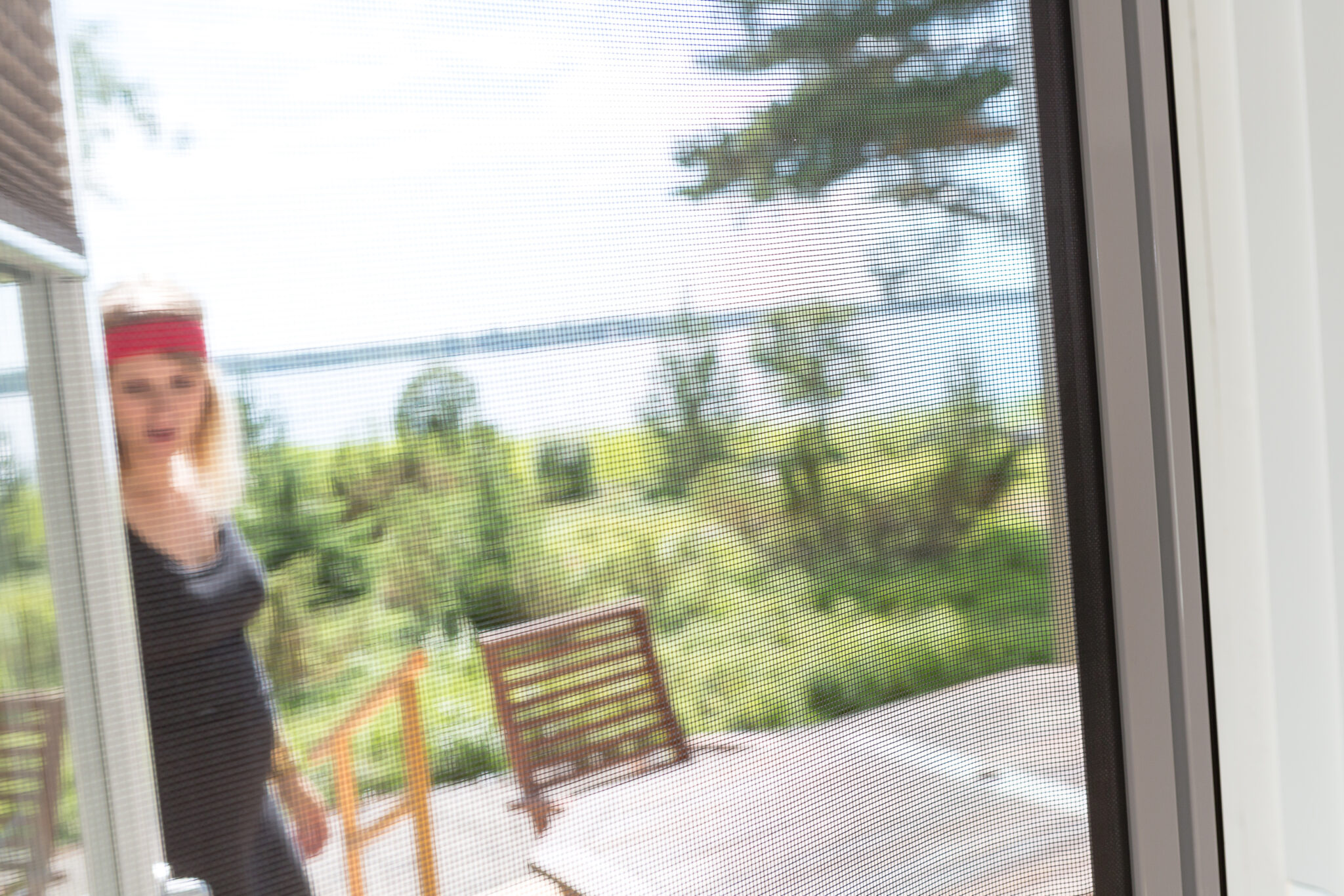 View through a patio insect screen door showing a woman outside on a terrace, with mesh clearly visible and keeping insects from entering