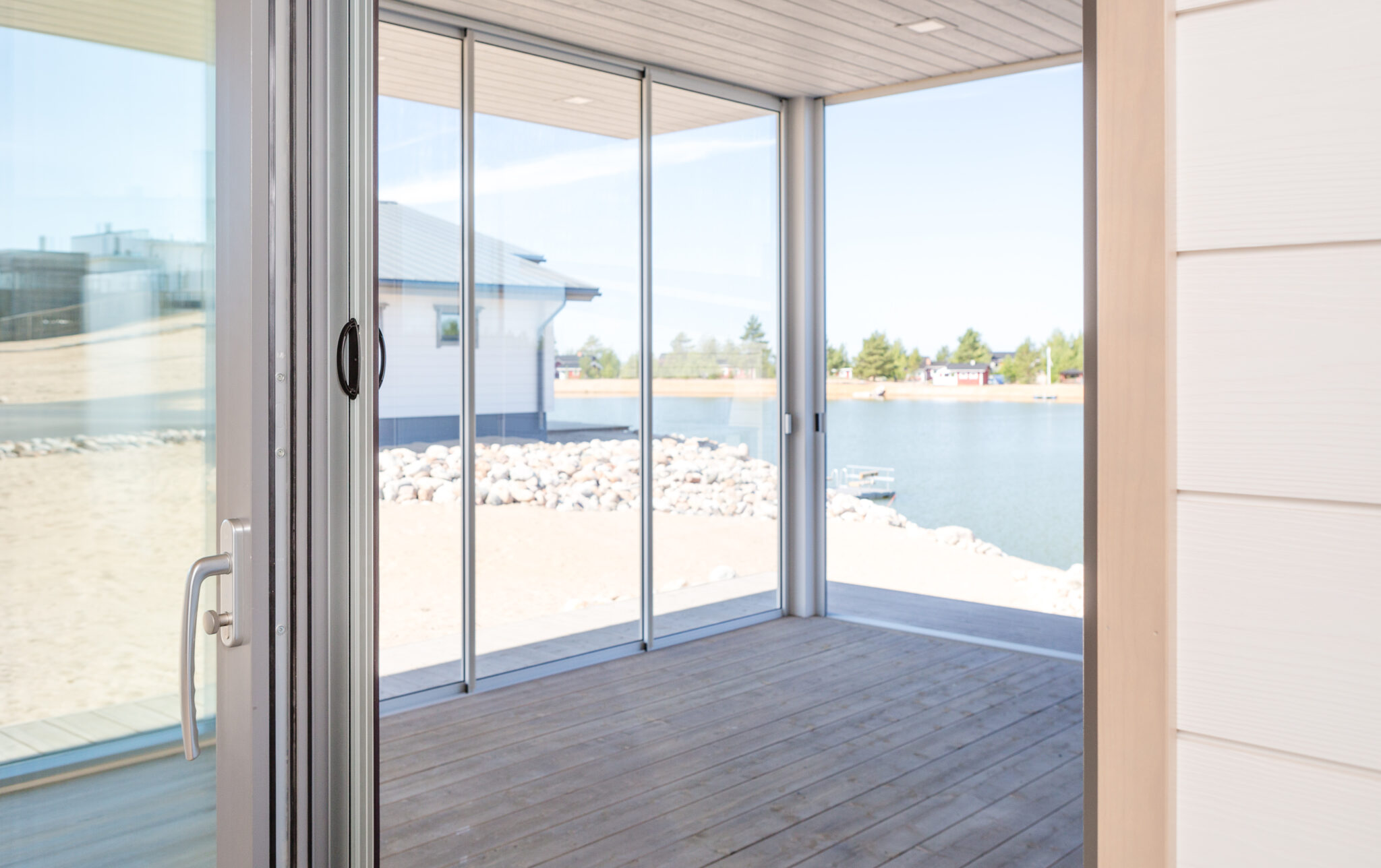 Open doorway leading to a covered terrace with large glass panels and a lake view, featuring a retractable insect screen door integrated into the frame