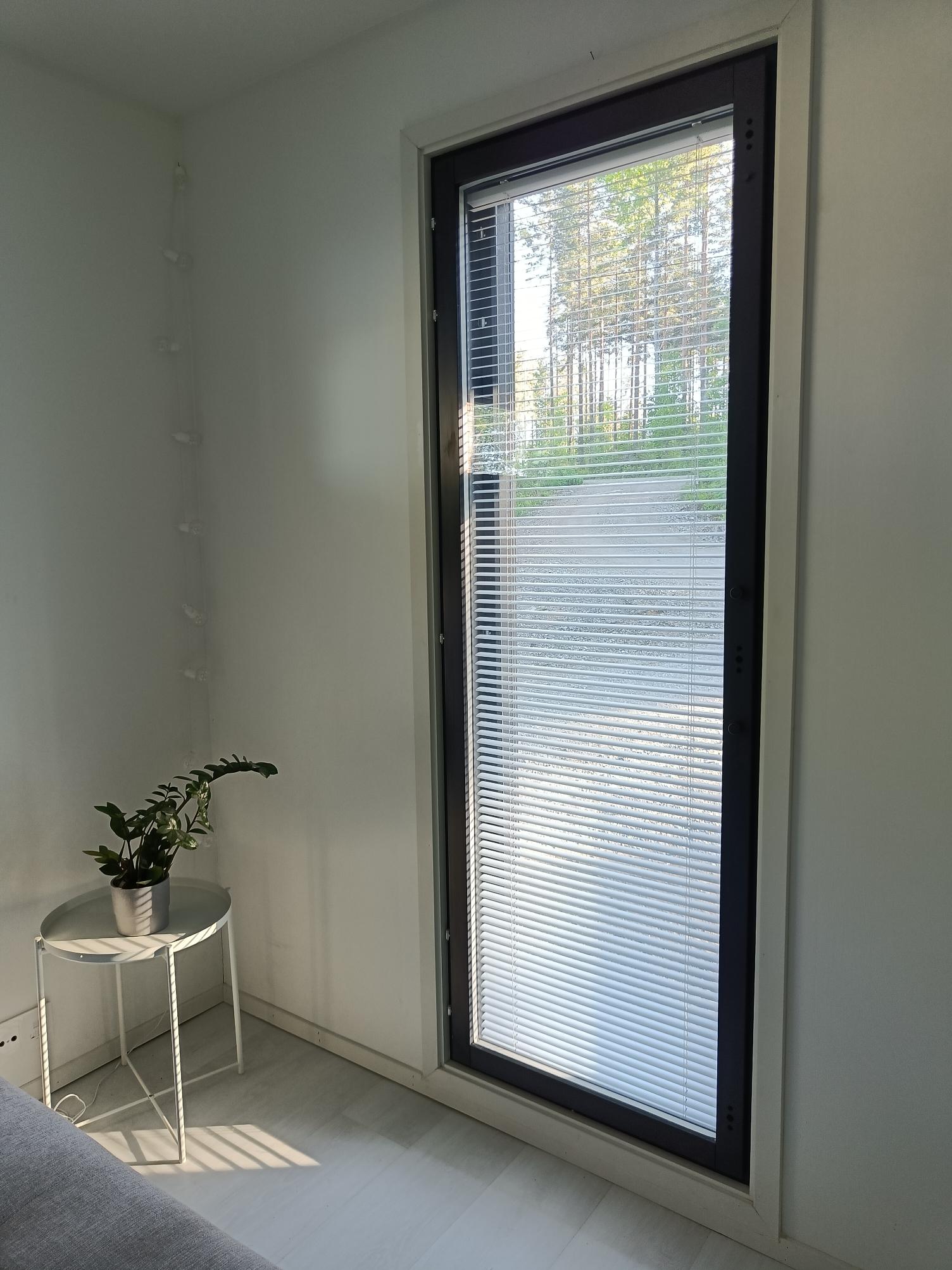 Tall window door with venetian blinds filtering daylight, creating soft shadows in a clean and minimalist interior