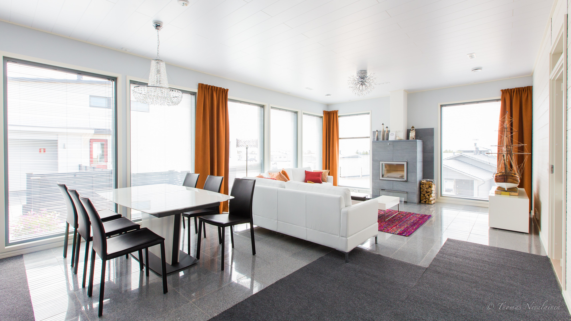 Bright open-plan living room with large windows, venetian blinds and orange curtains creating a clean and airy atmosphere
