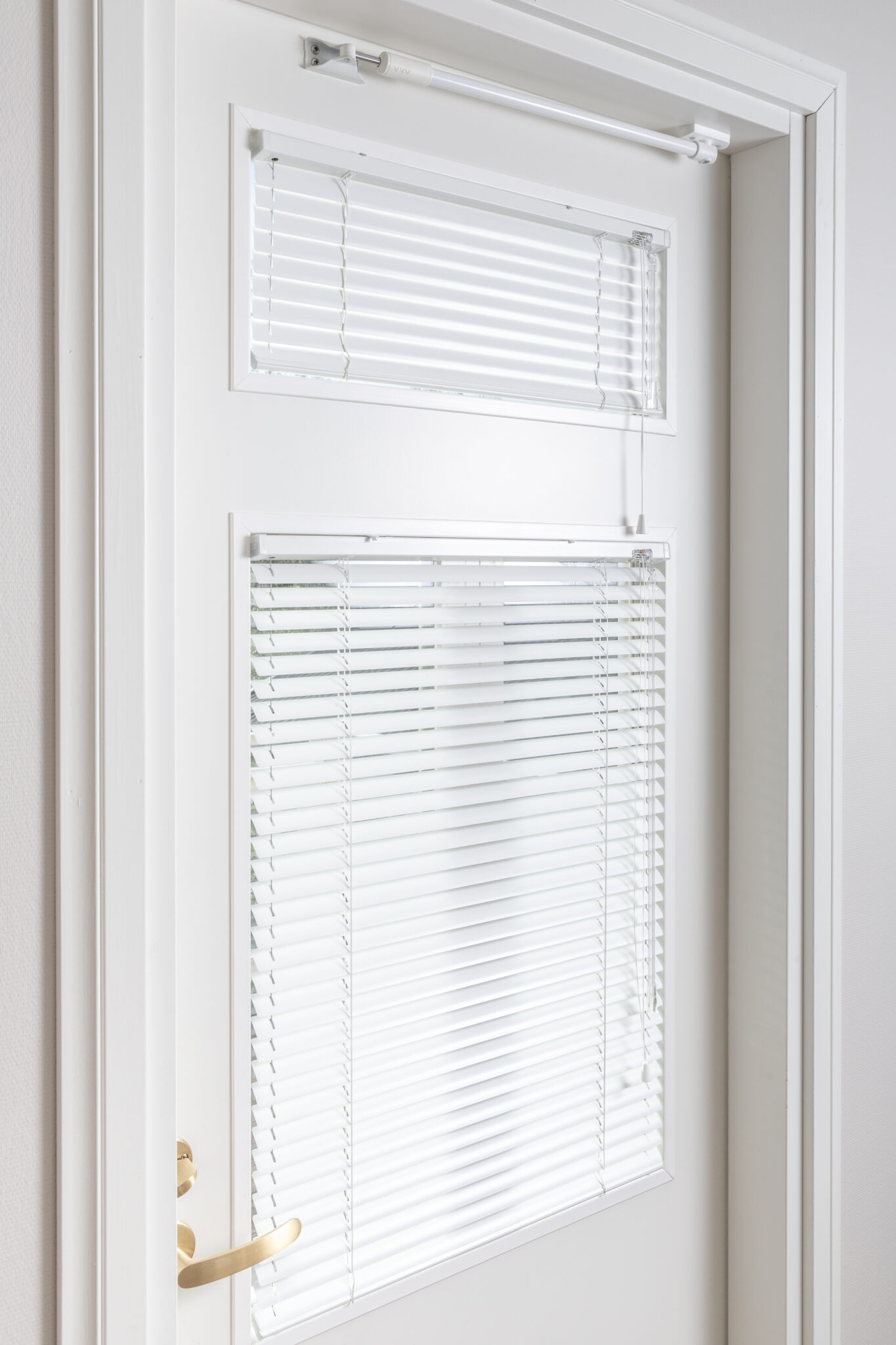 Close-up of a white door with two glass panels fitted with white venetian blinds, showing tilt controls and a clean, minimal finish