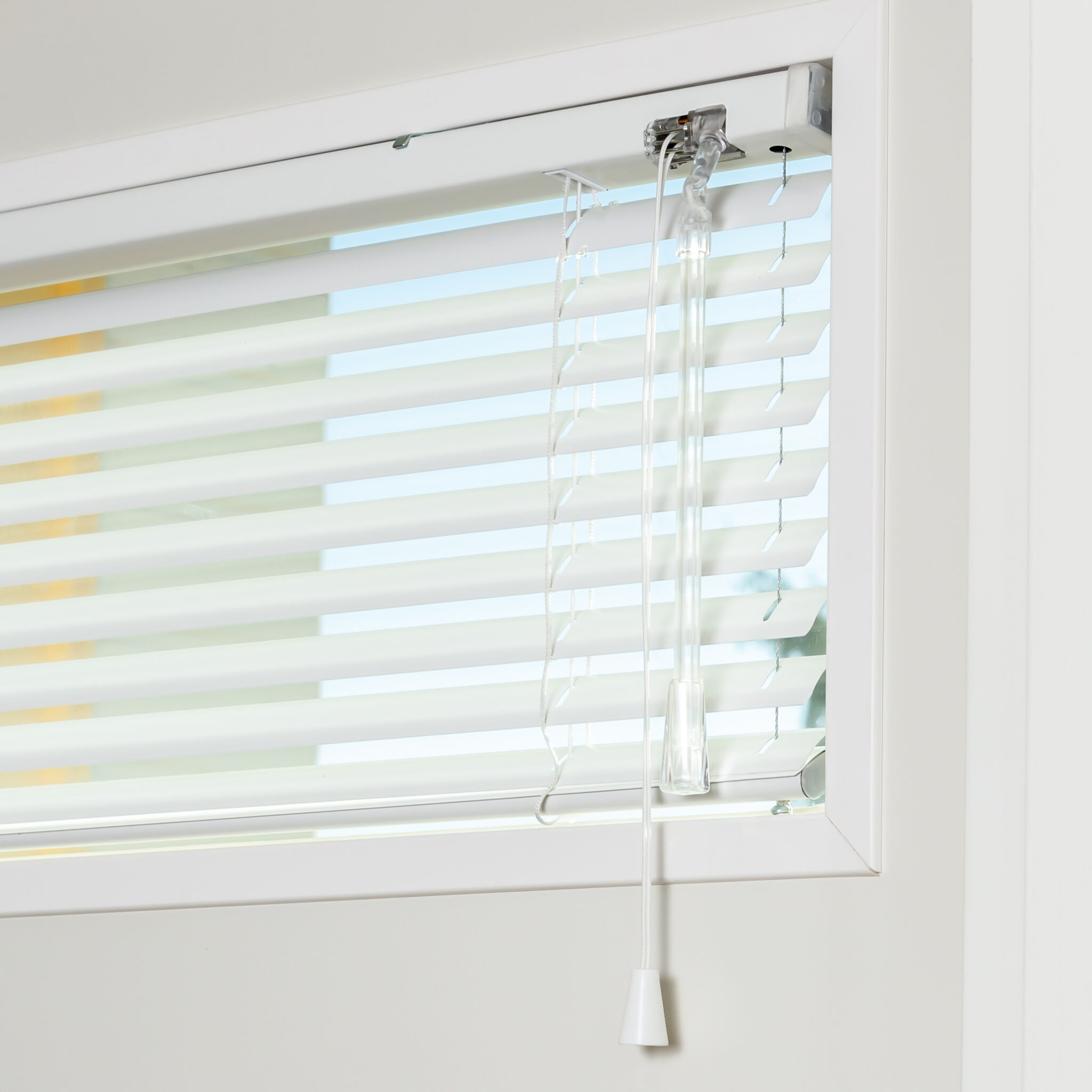 Close-up of white venetian blinds installed inside a window frame, showing the tilt wand and control cord for adjusting light and privacy